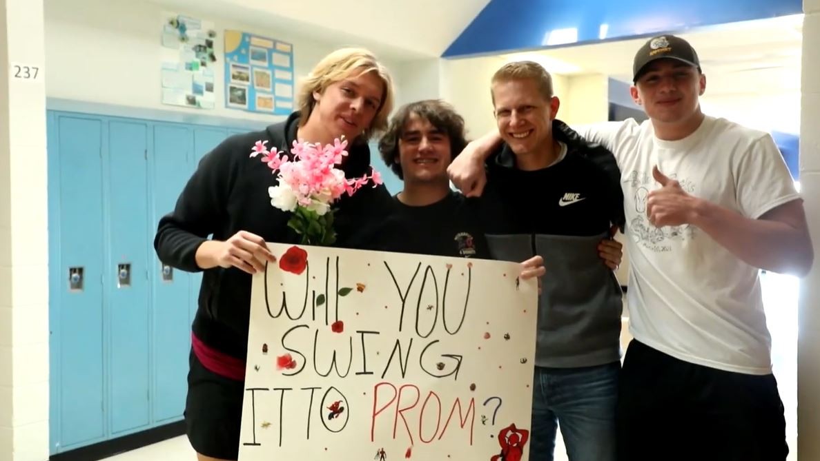 Three students ask Mr. Abbott to prom with a sign saying, "Will you swing it to prom?"